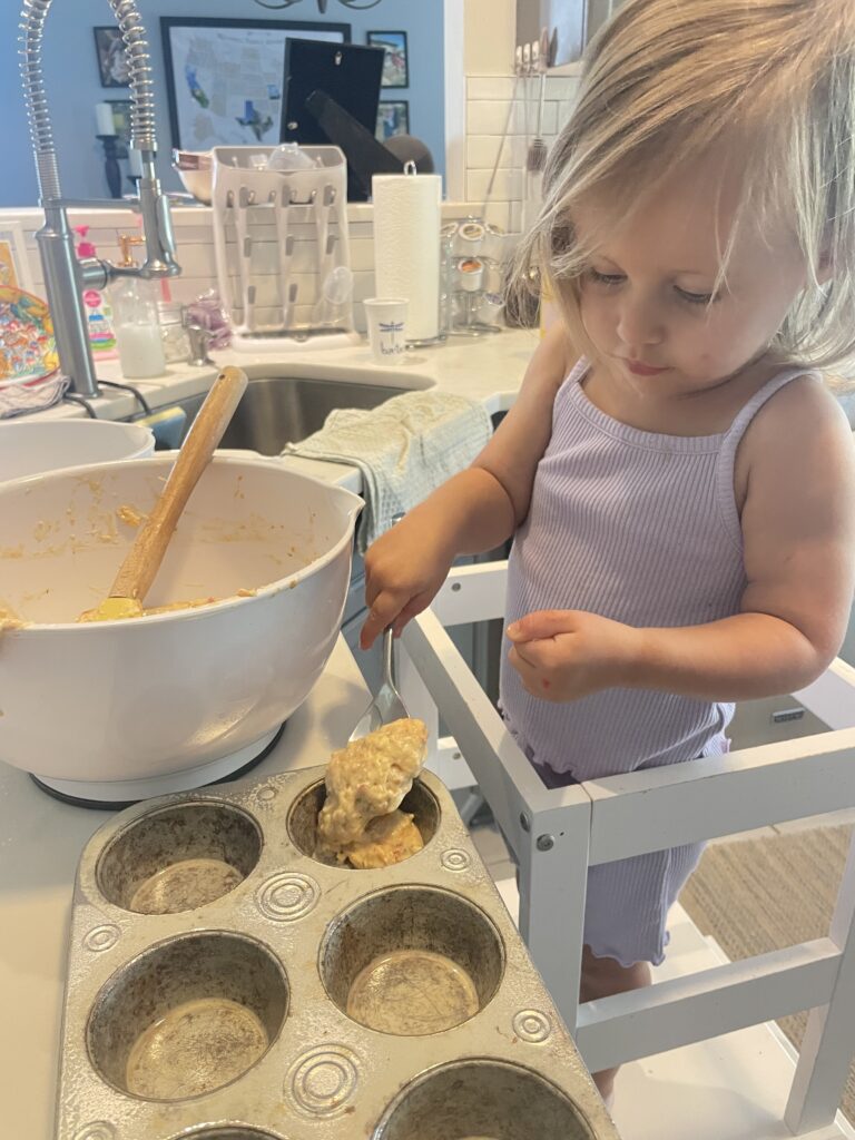a small toddler girl in the kitchen baking Hidden veggie pizza muffins perfect for toddlers topped with cheese and pepperoni 