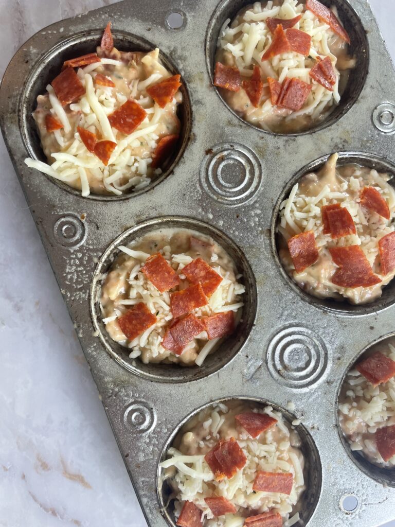 Hidden veggie pizza muffins perfect for toddlers topped with cheese and pepperoni in a muffin pan before they go in the oven.
