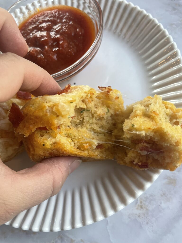 Hidden veggie pizza muffins perfect for toddlers topped with cheese and pepperoni pulled open to show how cheesy they are inside!